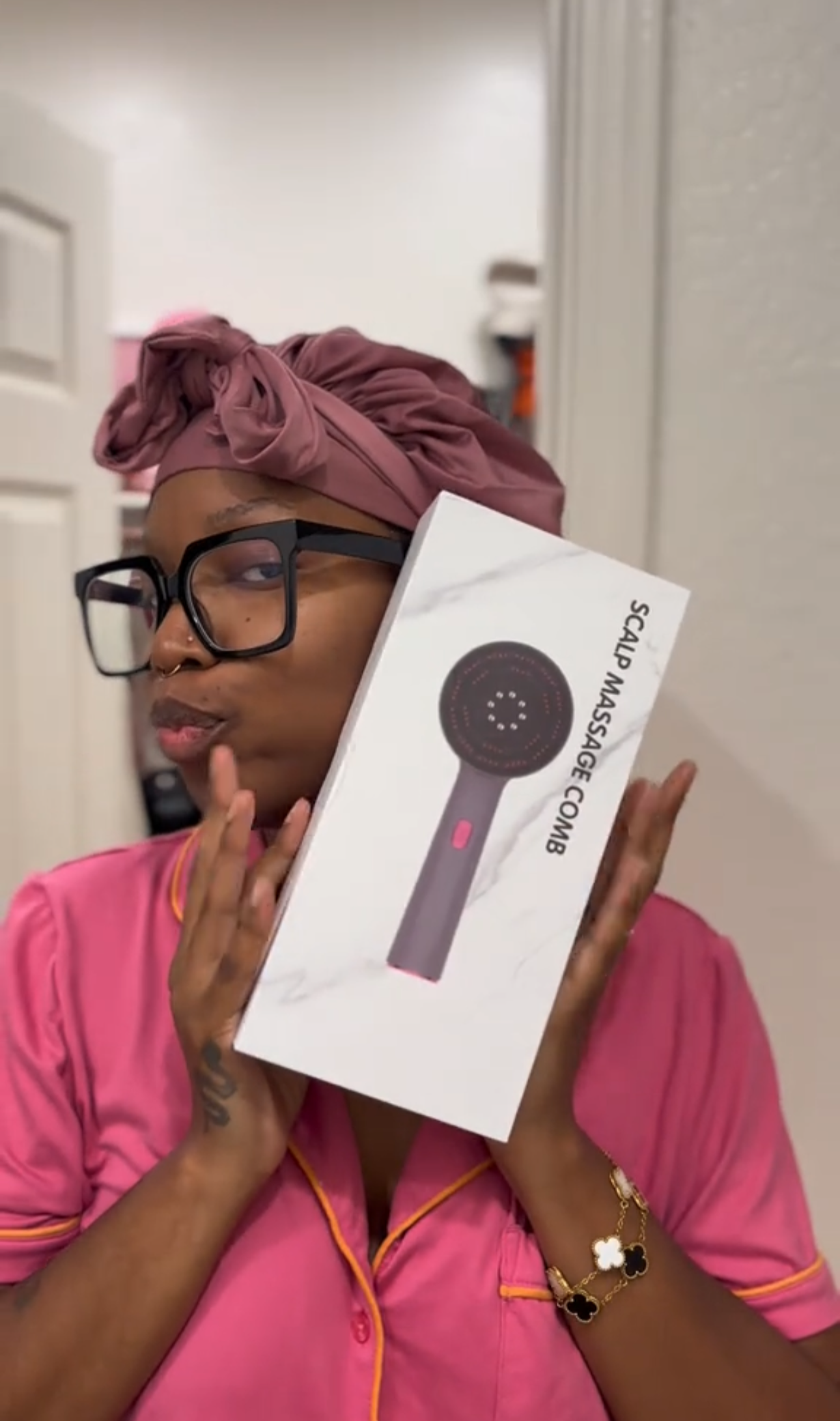 A woman holding a white box with a scalp massager device image printed on it, wearing a pink shirt.